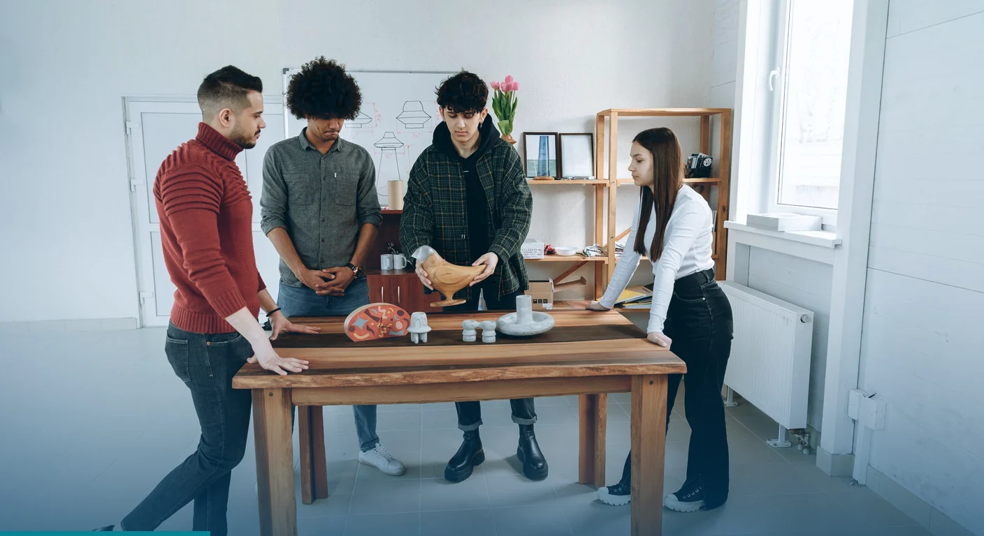Creative team gathered around a wooden table, examining product prototypes in a bright studio