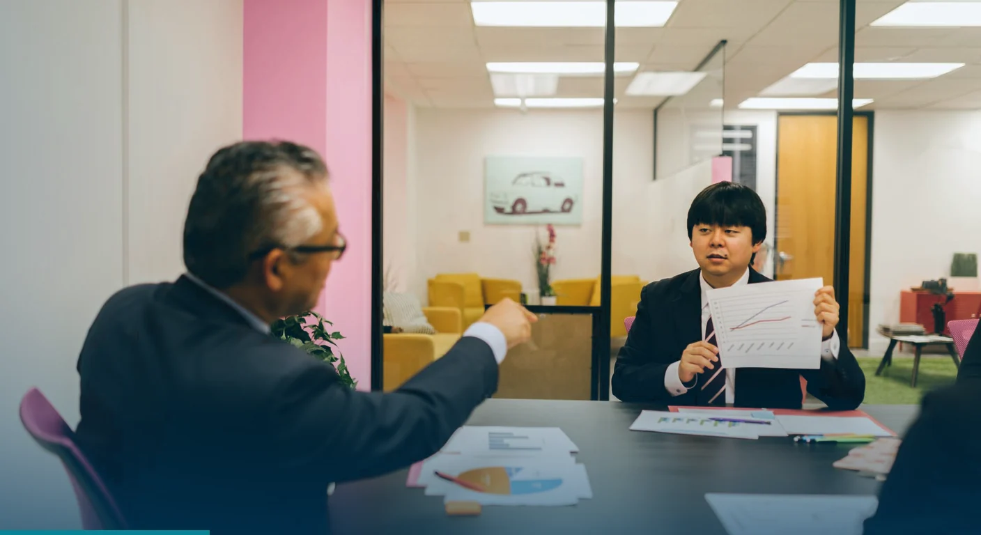 Colleague holding up a printed chart in a meeting while another points at it