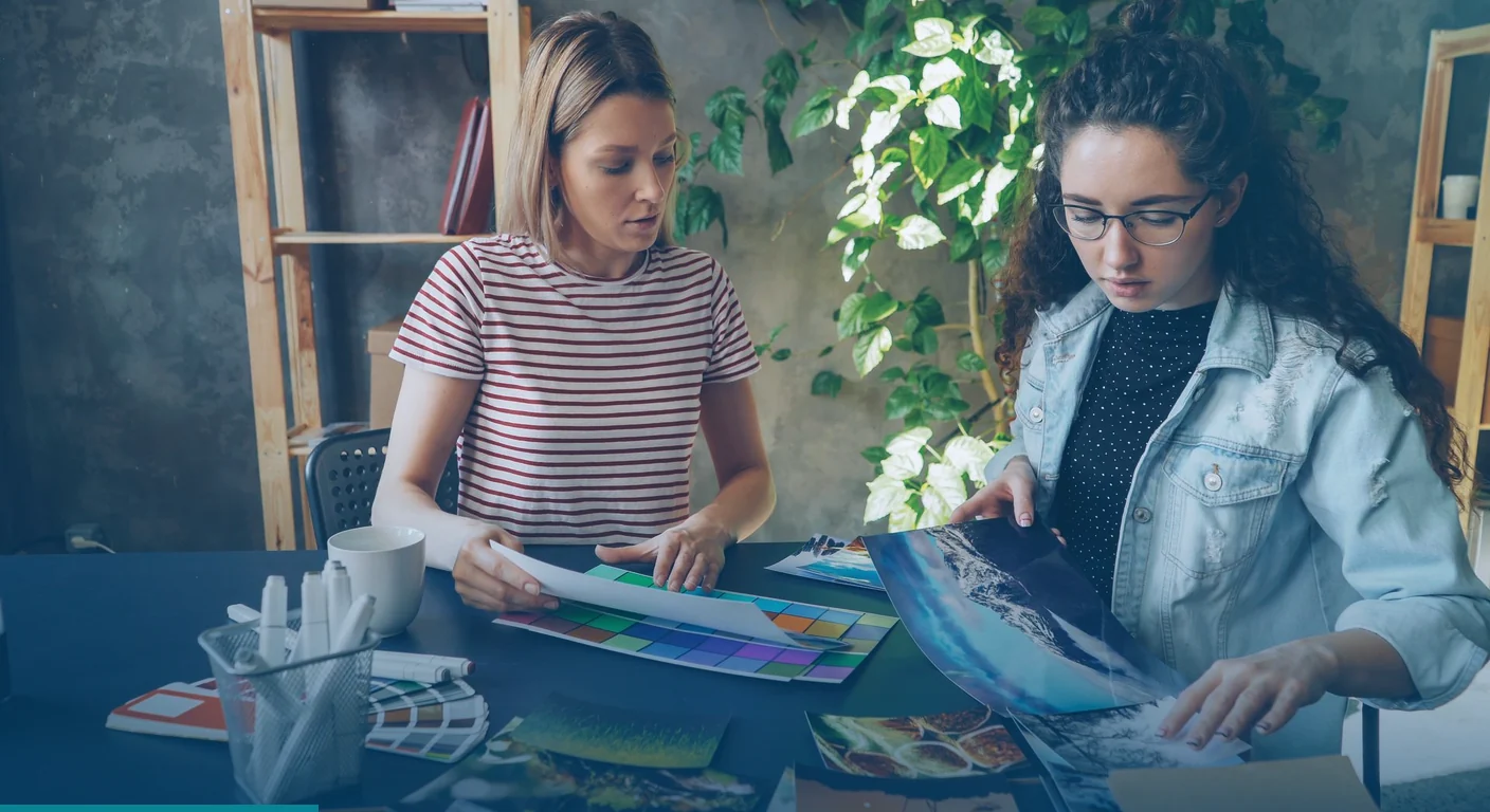 Two designers comparing colour swatches and printed photos at a studio desk