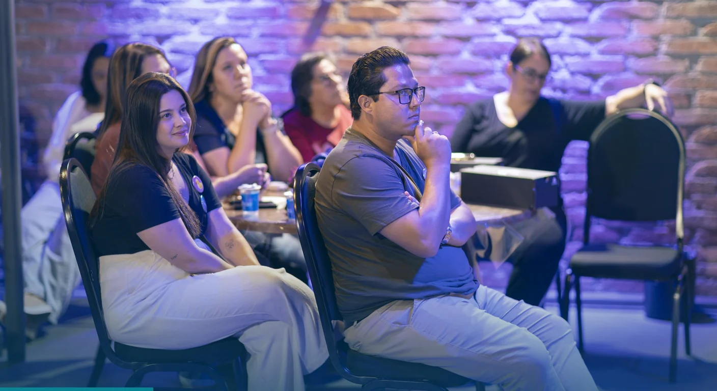 Attendees seated in a brick walled room, listening closely to a session