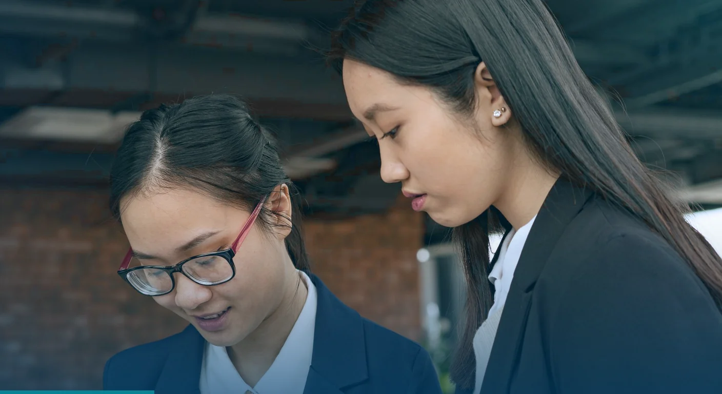 Two colleagues in blazers looking down together at content they are reviewing