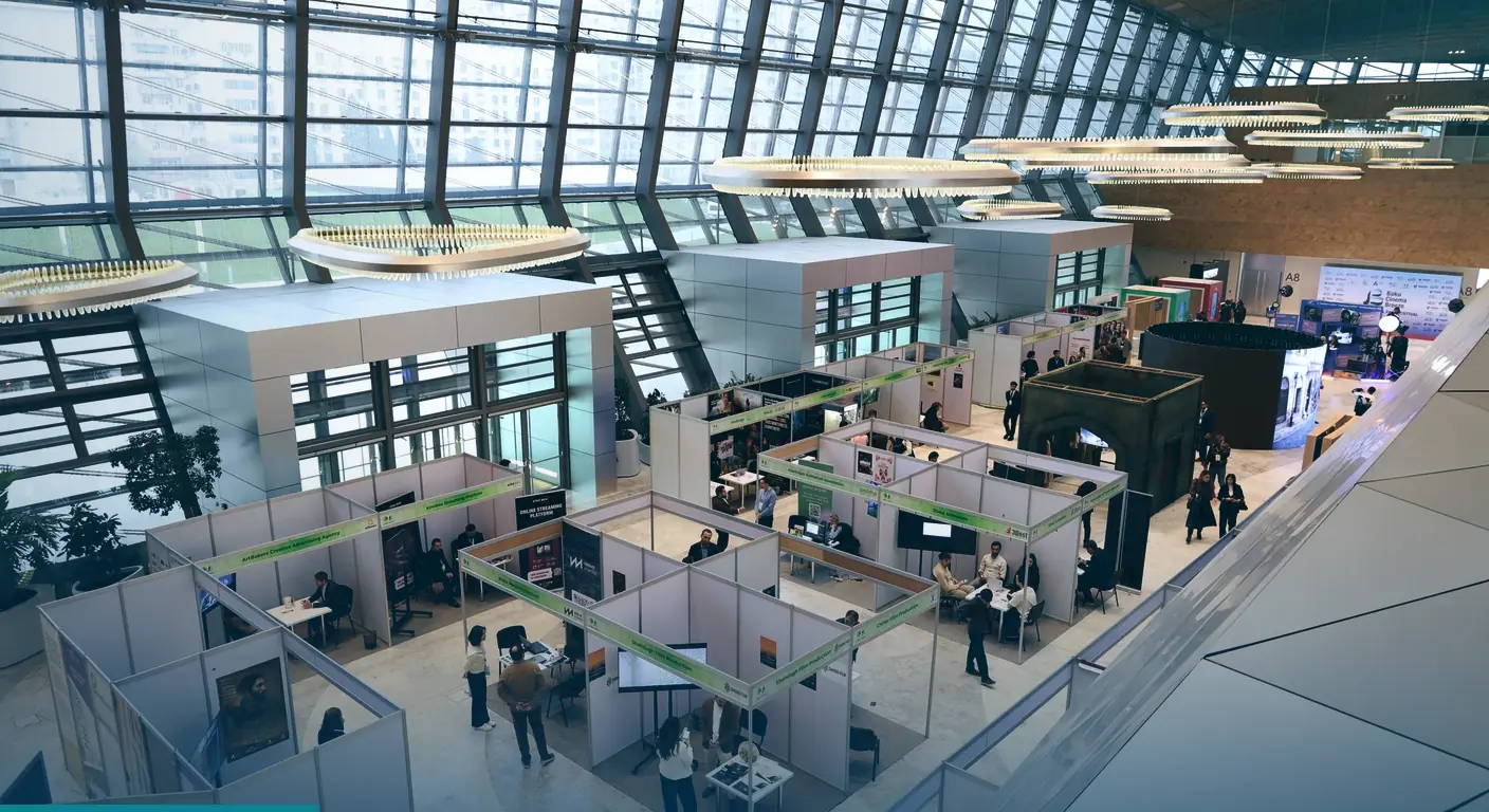 Trade show hall with rows of exhibitor booths under a high glass roof