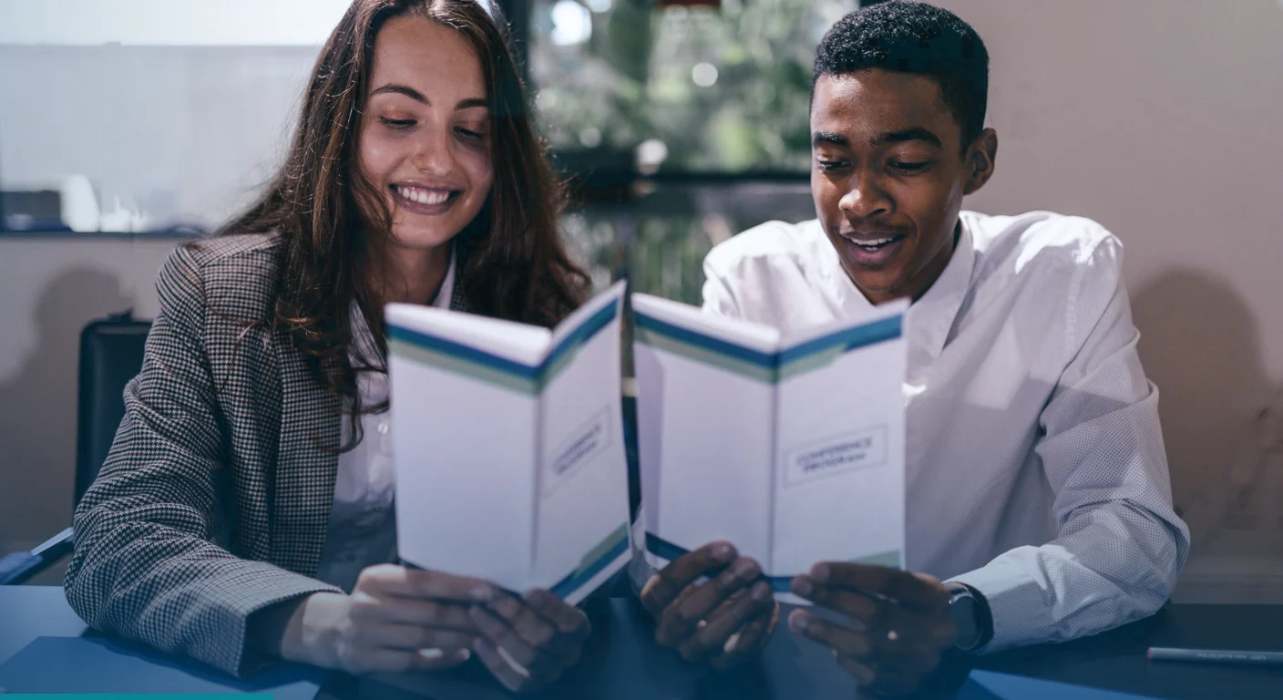 Two guests smiling as they read folded event programmes at a table