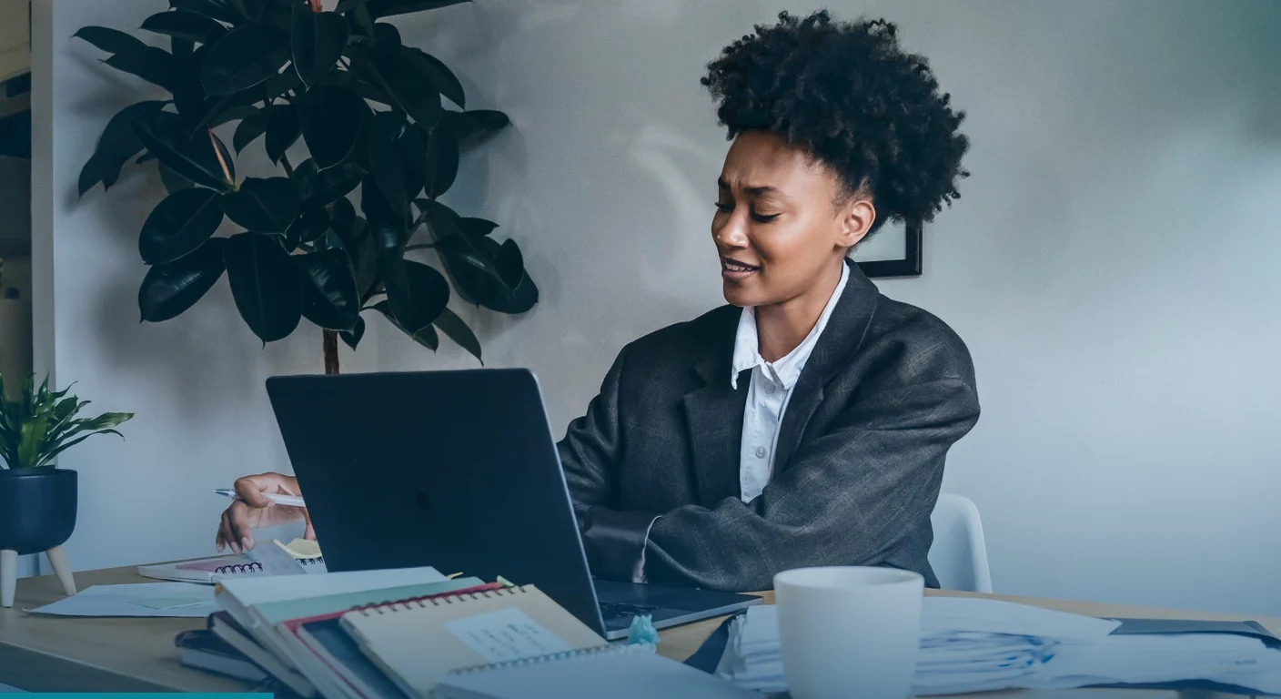Professional in a blazer talking to her laptop at a desk stacked with notebooks