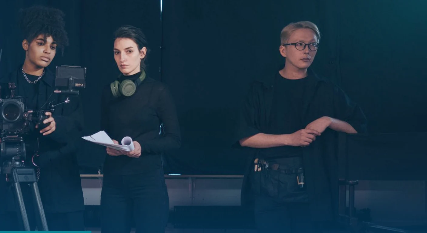 Video crew in black with a camera rig and script, standing ready on set