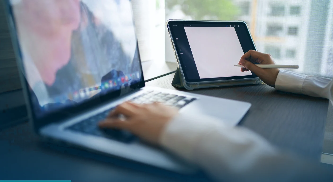 Person working on a laptop while sketching on a tablet with a stylus