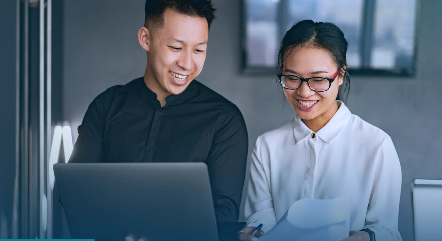 Two smiling colleagues reviewing work on a laptop, the kind of teamwork behind creative as a service