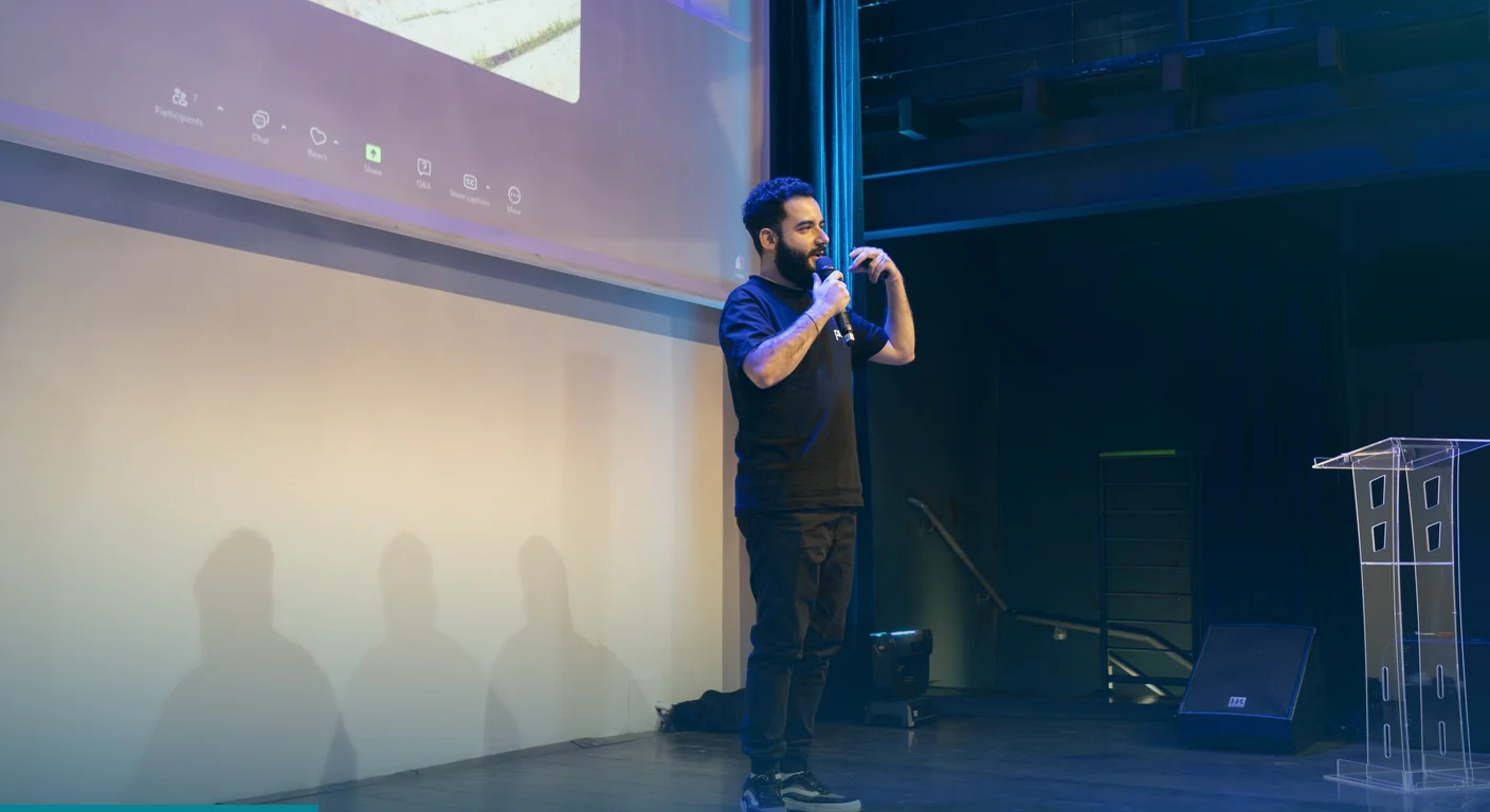 Speaker with a microphone on stage in front of a projection screen, the kind of session a hybrid event platform can share