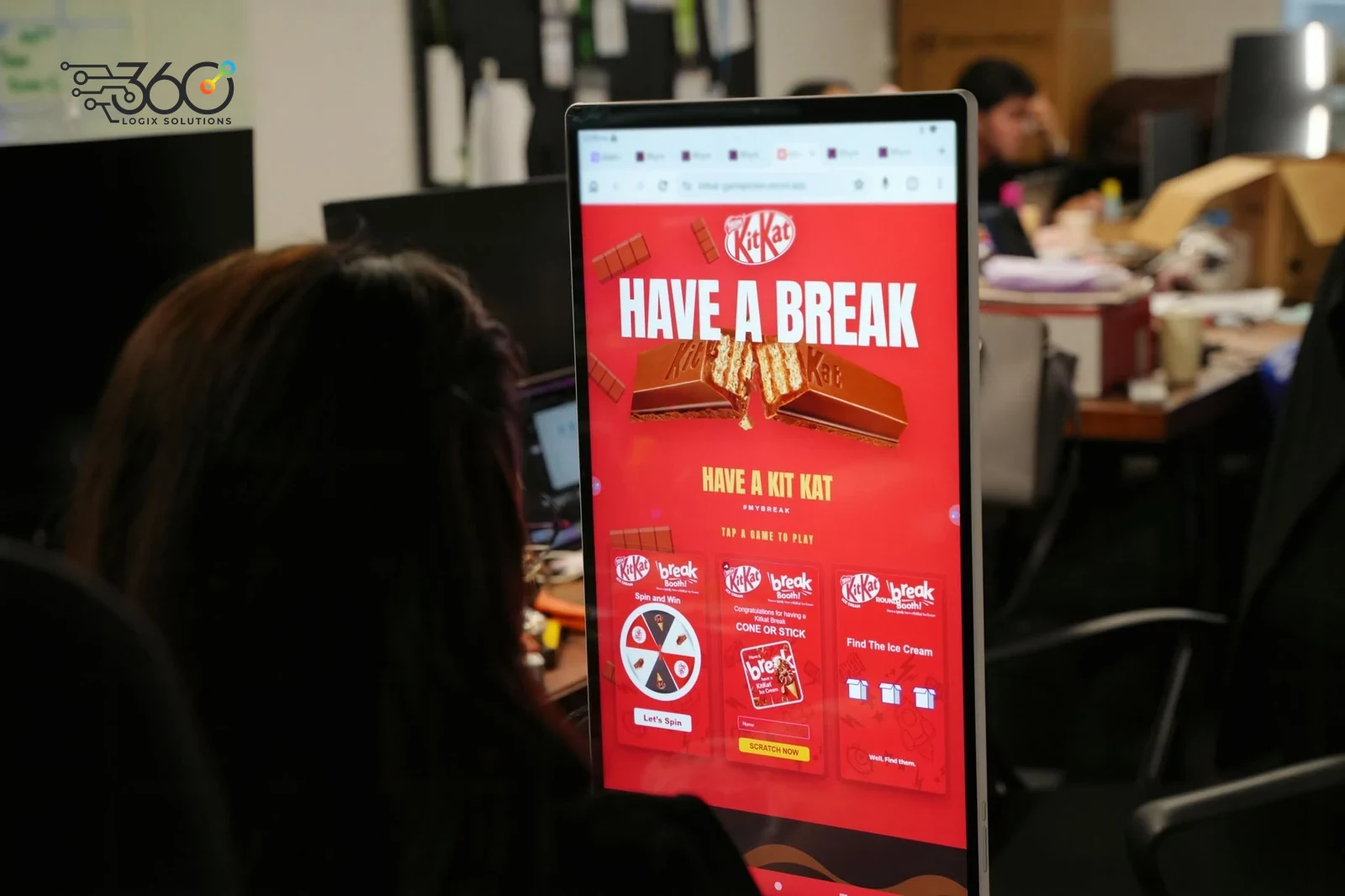 A 360 Logix team member, seen from behind, testing our KitKat game picker on a portrait touch-screen kiosk in the studio