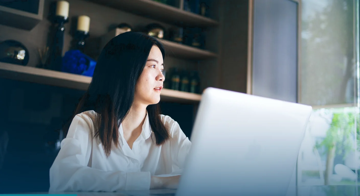 Woman at a laptop in a home office, glancing up from her screen