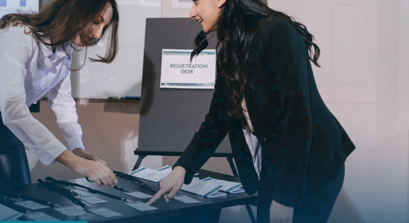 Two women arranging name badges and lanyards on a registration desk