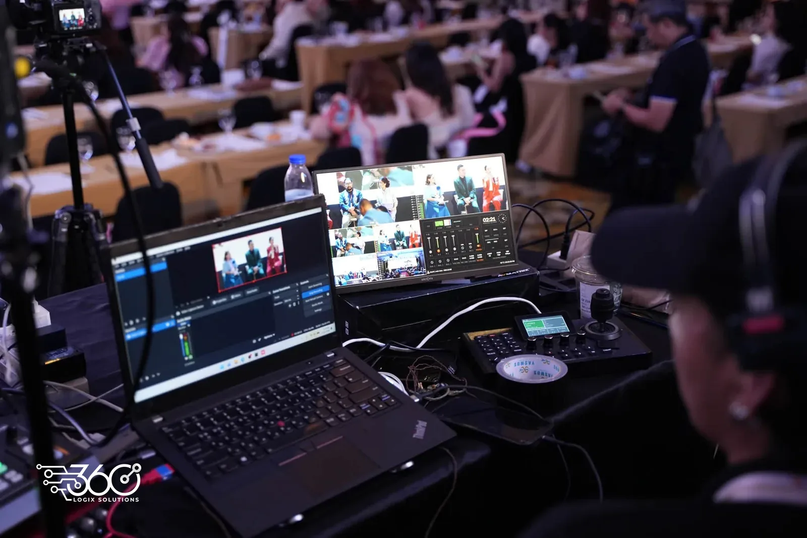 Live feed desk at the PAPSHPI Aesthetic Summit 2026 with laptops, a multiview monitor and a streaming control panel showing the session on stage, with an operator in a headset beside it.