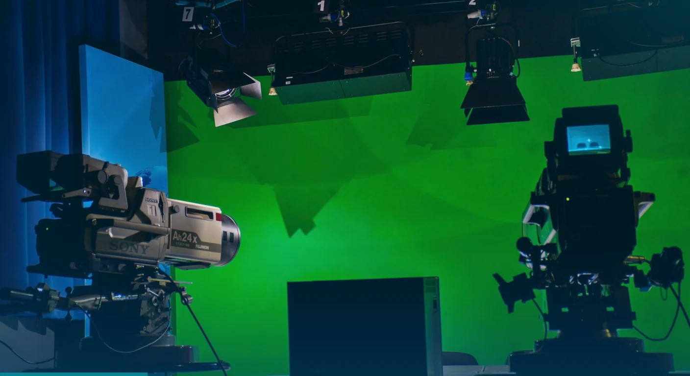 Television studio with a green screen, overhead lights and two broadcast cameras